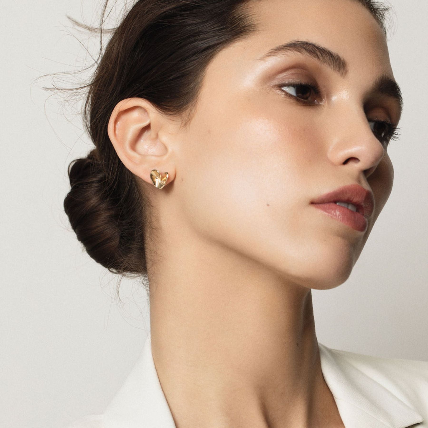 Model wearing organically textured folded heart stud earrings in 14 karat yellow gold