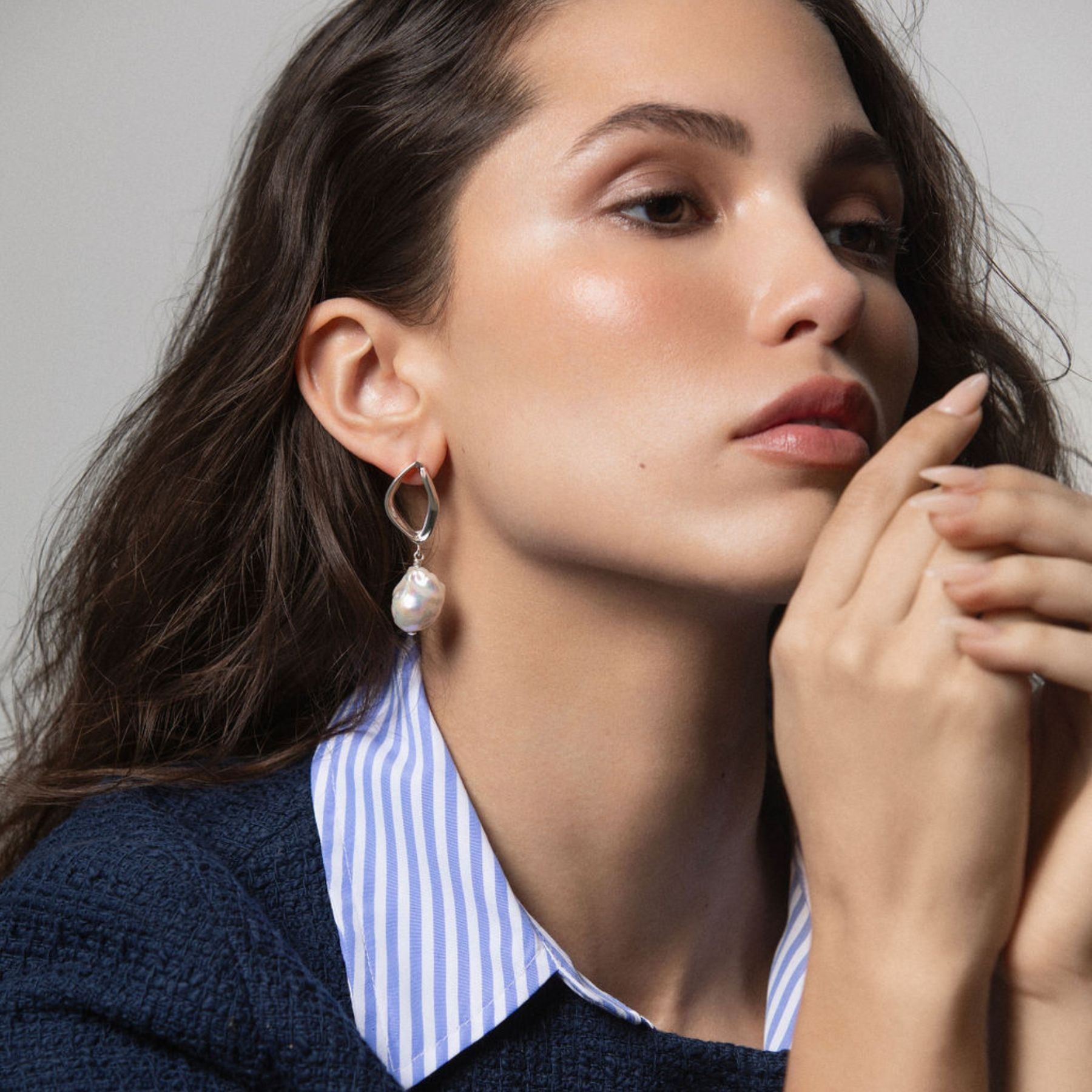 Model wearing a pair of abstract earrings in sterling silver with a baroque pearl drop.