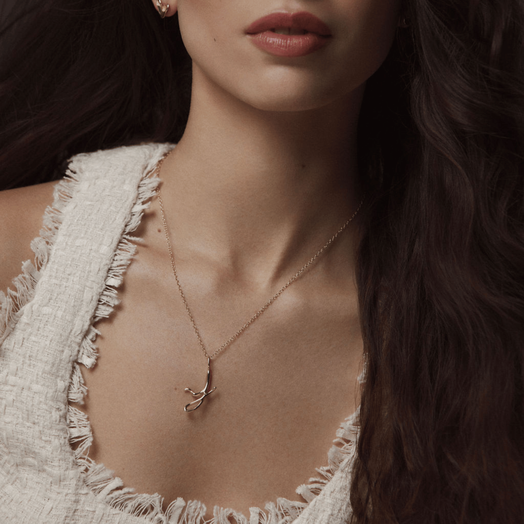 Model wearing a cursive initial J pendant in 14k gold.