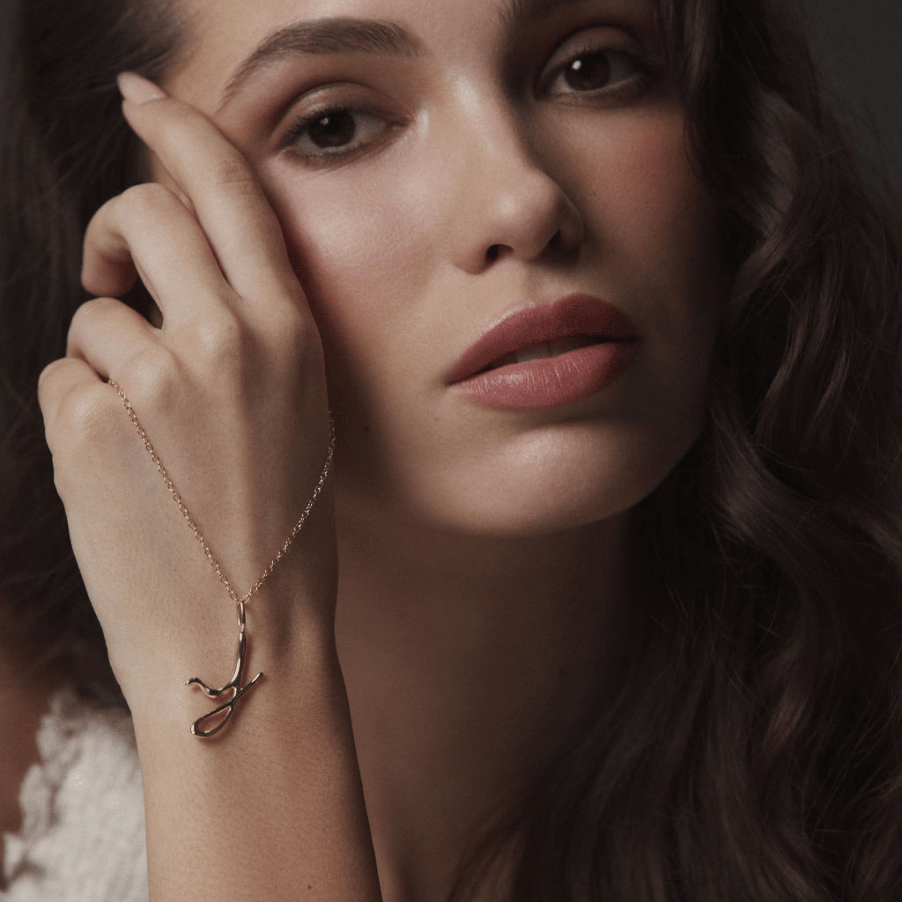 Model holding a cursive initial J pendant in 14k gold.