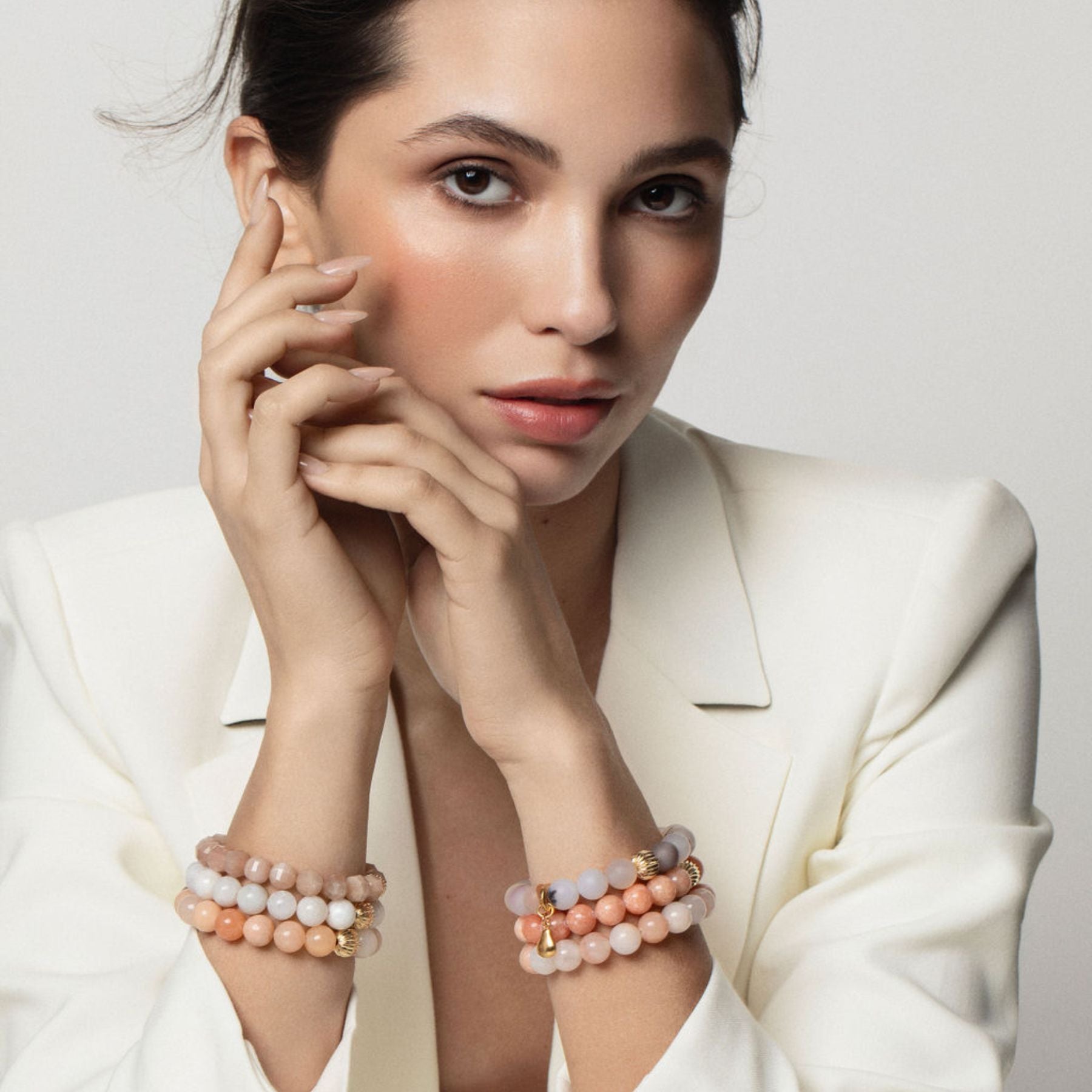 Model wearing stack of beaded bracelets in peach hues.