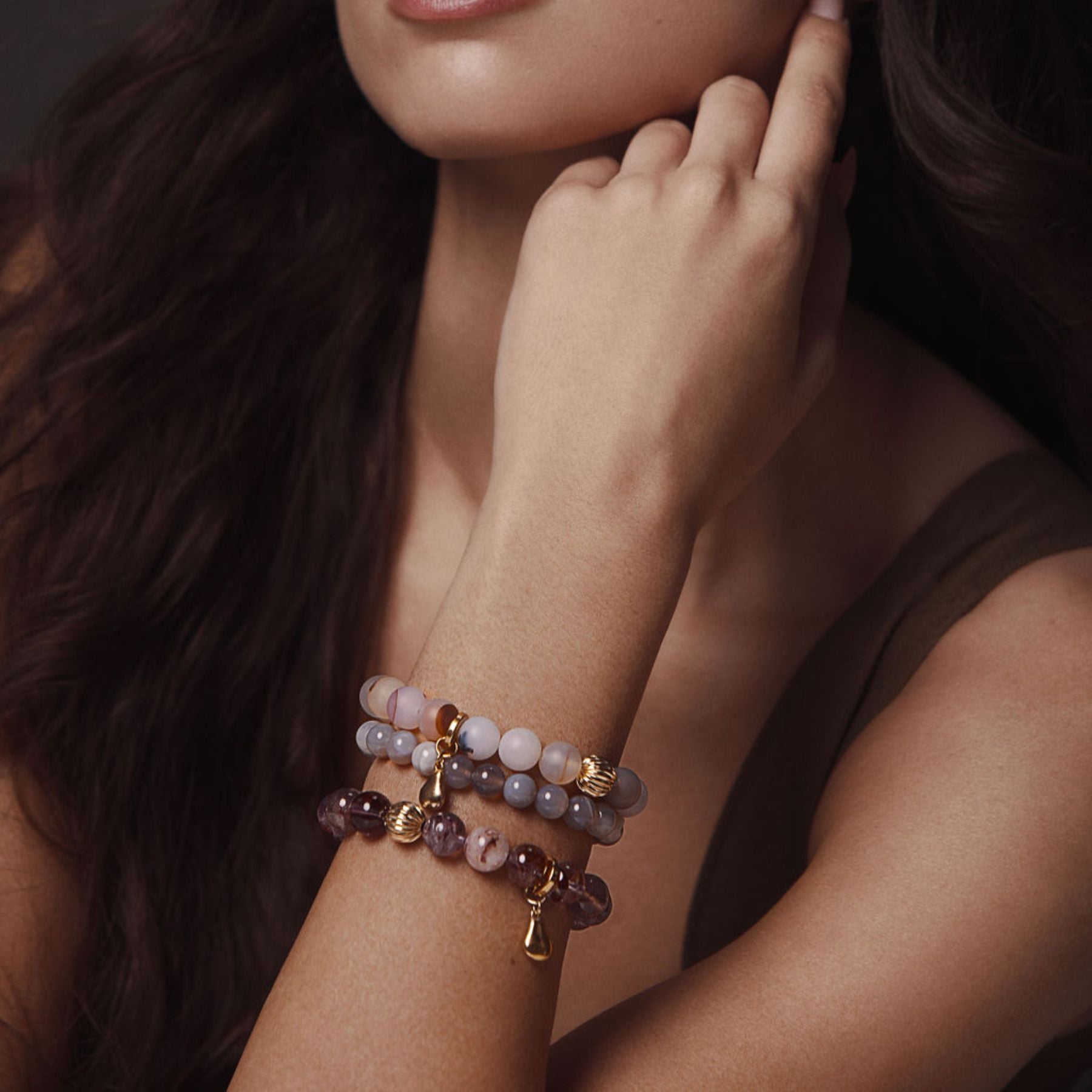 Model wearing stack of beaded bracelets in hues of purple and gray.