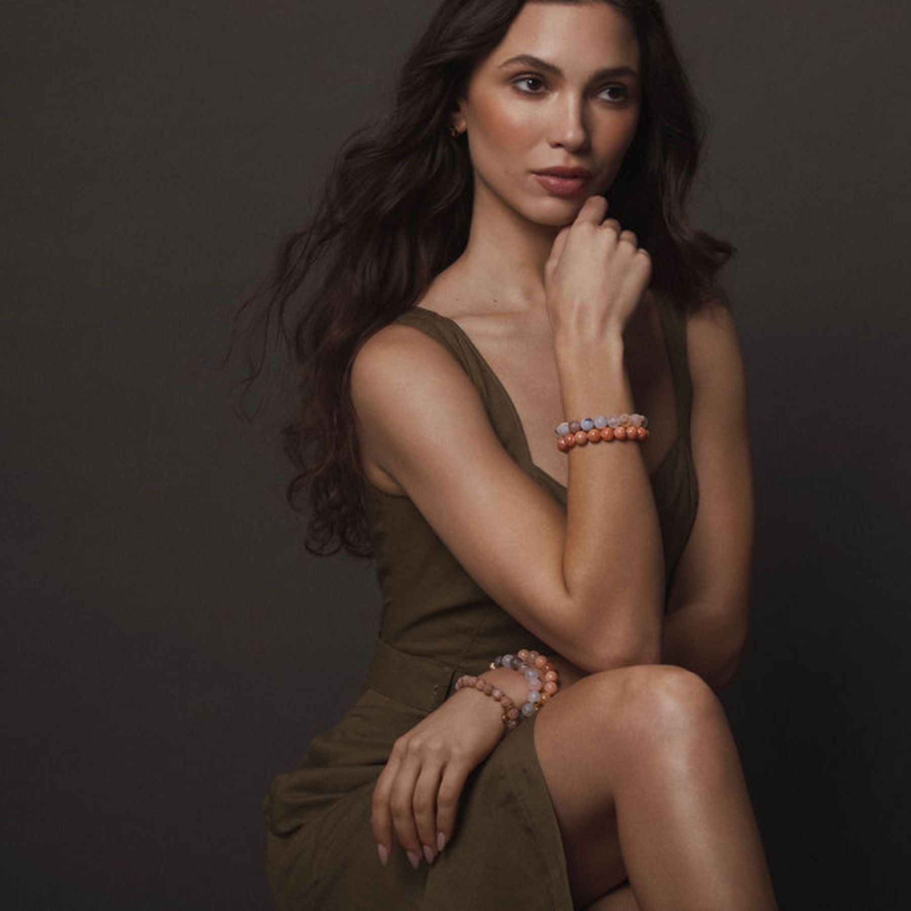 Model wearing stack of beaded bracelets in gray and orange hues.