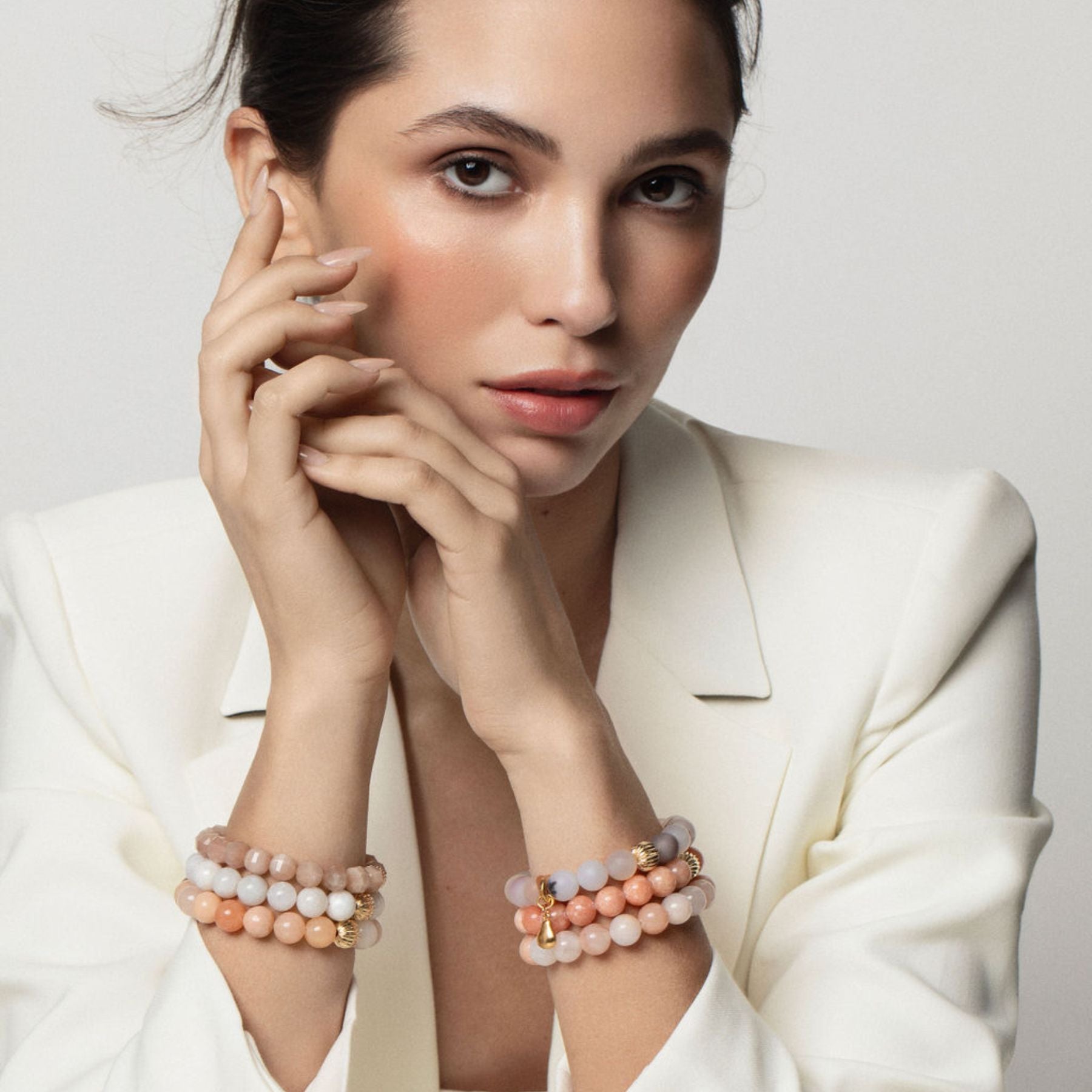 Model wearing stack of beaded bracelets in gray, white, and peach hues.