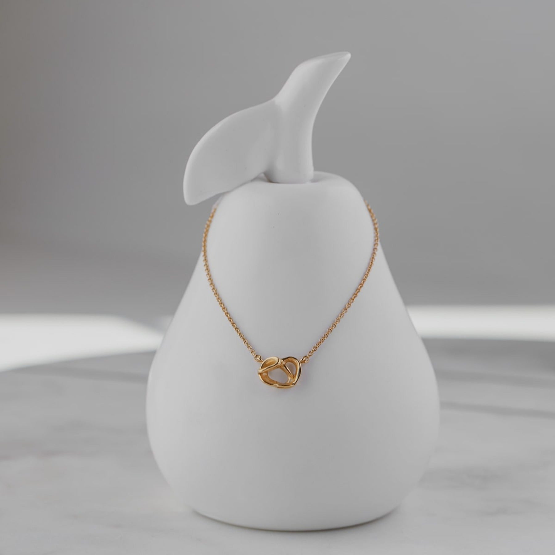 Abstract pretzel pendant necklace on a delicate cable chain finished with an Anjou pear charm in 18k gold vermeil.